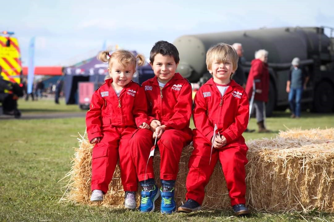 Children sit on hay in Red Arrows Pilot uniform.